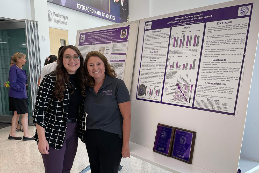 Two women stand in front of a research poster.