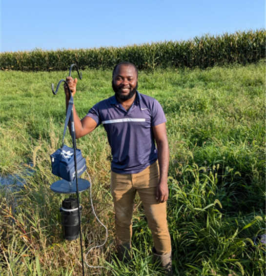 Man standing in an open field holding up an insect trap