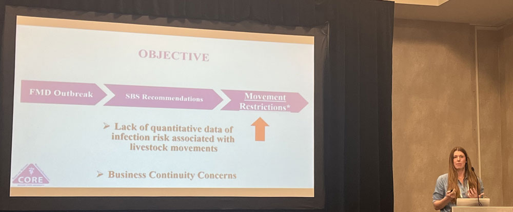 Torre speaking at a podium to audience members with a slide projected next to her.