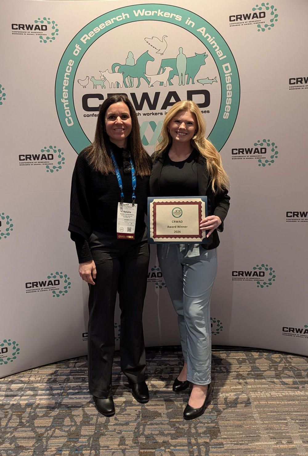 Taylor holding an award and standing with Dr. Cernicchiaro in front of the CRWAD step and repeat