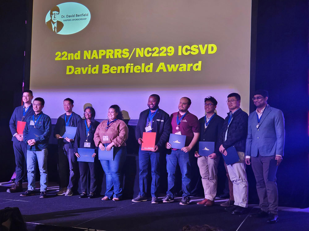Group photo of award winners holding their awards in on a stage in front of a projected slide