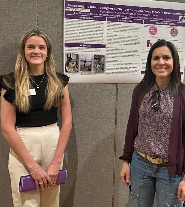 Two women standing in front of a divider with a poster